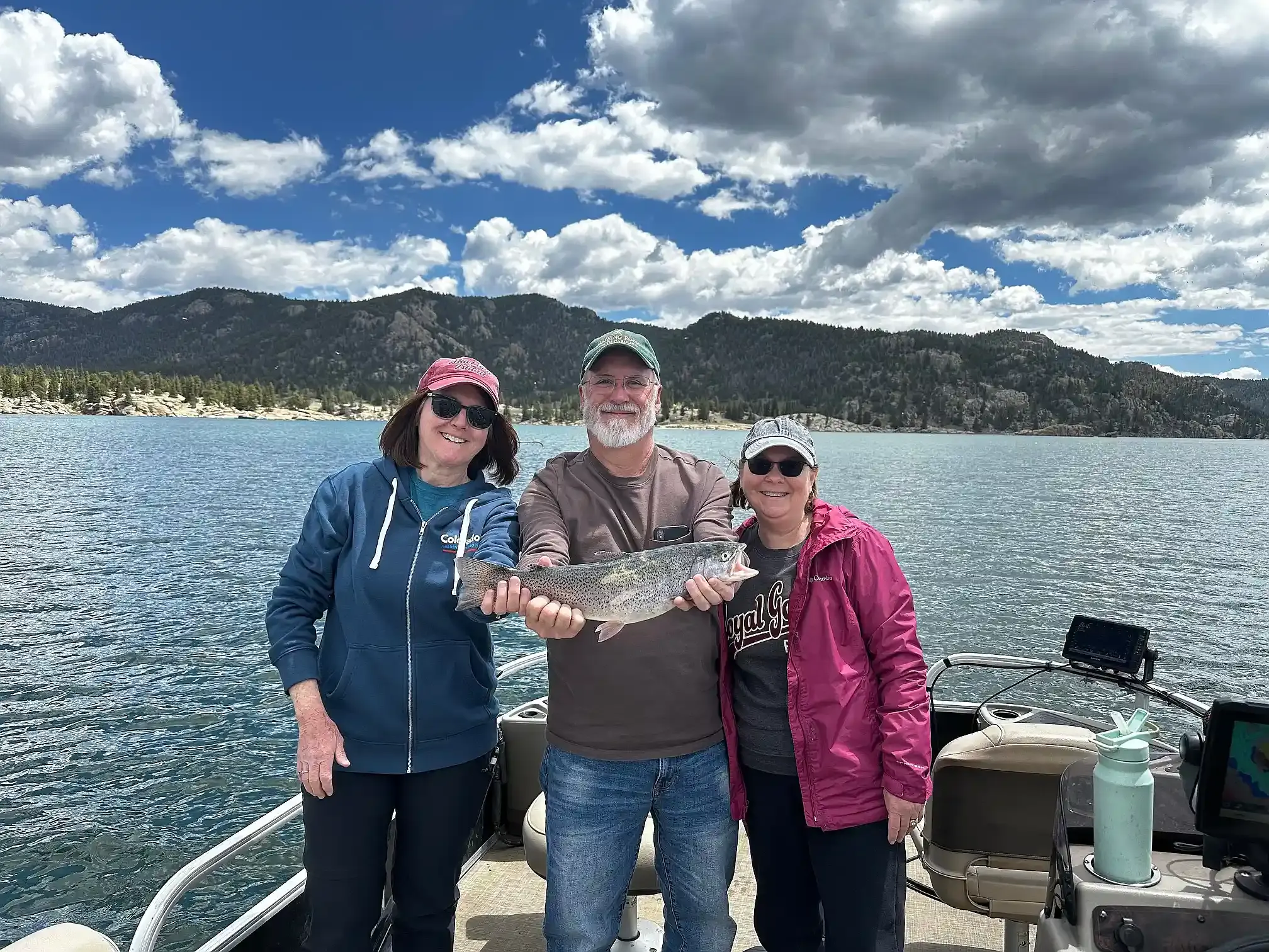 Two women and a man holding a rainbow trout aboard the pontoon on Eleven Mile Reservoir