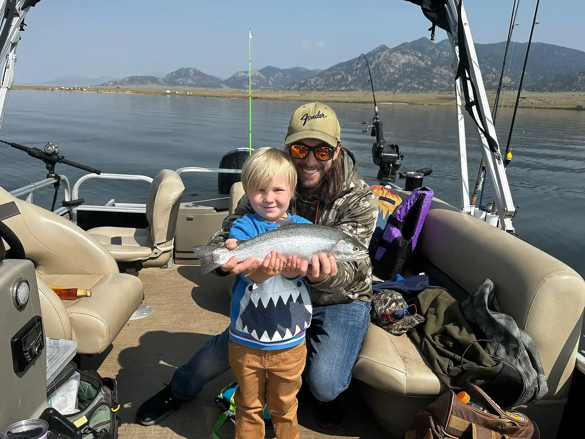A young angler holding a rainbow trout with help from his guide